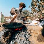 Scena Vivace nel Deserto del Thar, India: Santone Indiano Salta su una Pentola del Pane locale, Condividendo un Momento Unico con la Comunità Locale durante un Viaggio Indimenticabile."